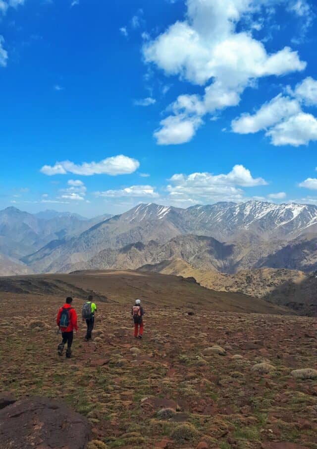 a group of people walking on a dirt path in front of a mountain range